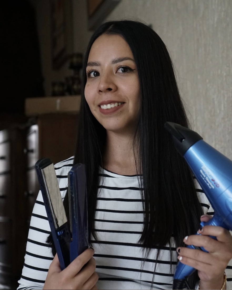 Eunice sonriendo con una plancha y una secadora en las manos